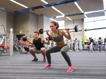 young man and woman training with barbell in gym
