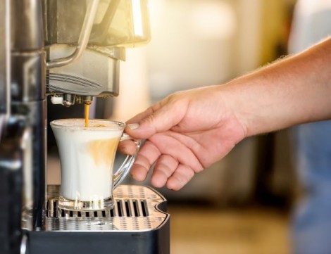 Hand taking coffee cup in automated coffee making machine.