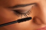 closeup of a young dark-skinned woman applying mascara on a whit